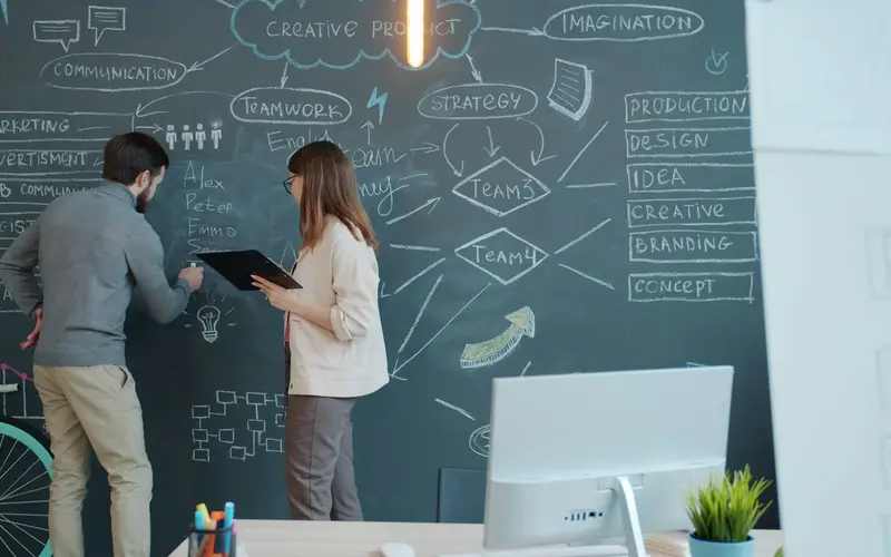 Two colleagues planning ideas on a chalkboard wall in an office