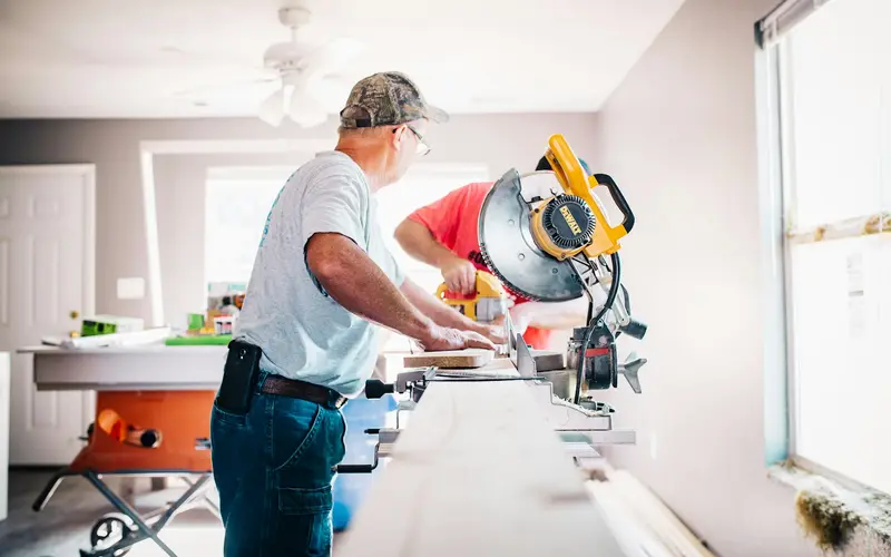 A handyman cutting trim on a miter saw inside a home