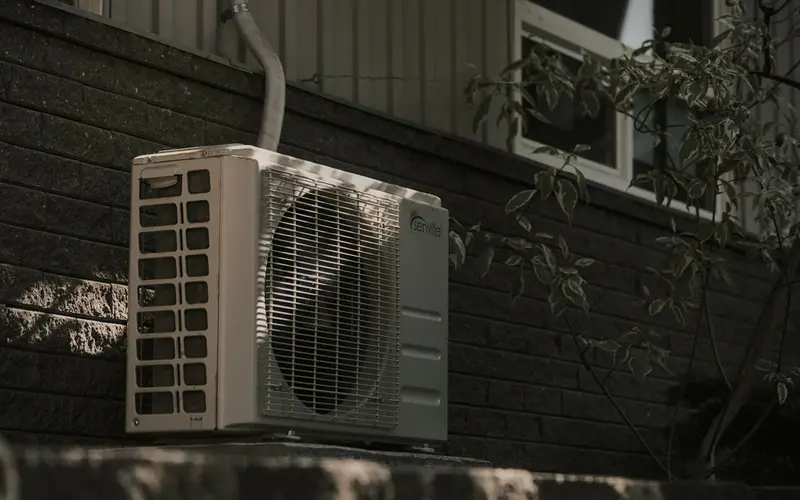 An outdoor air conditioning unit mounted on a dark brick wall