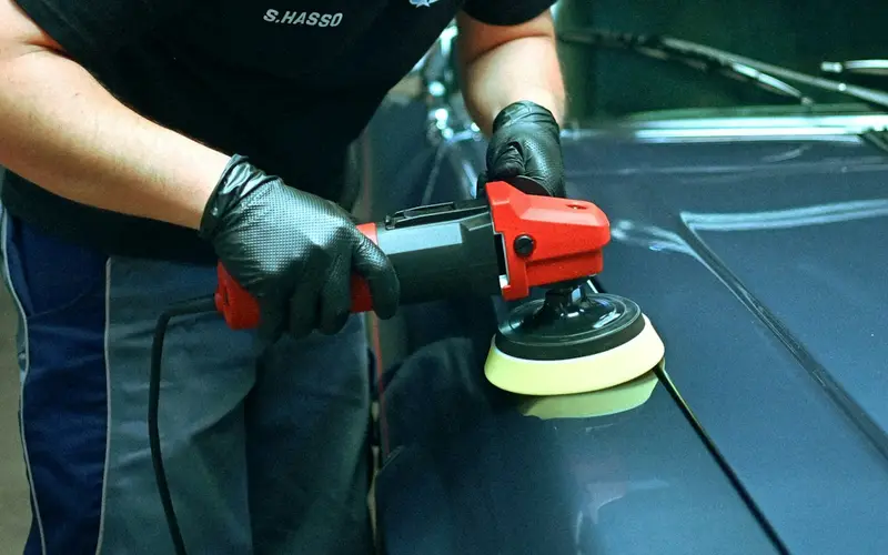 A detailer polishing the hood of a car with an orbital buffer