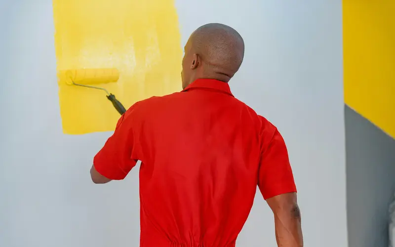 A painter rolling yellow paint onto a wall