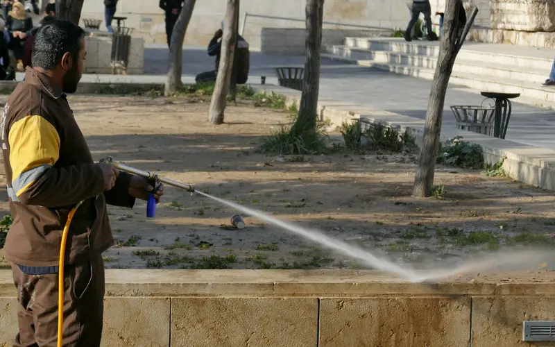 A worker pressure washing a paved area in a park