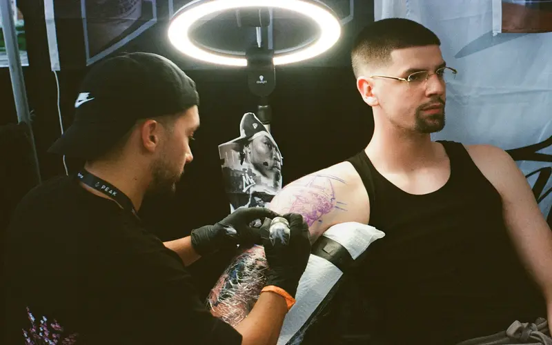 A tattoo artist working on a client's arm in a studio