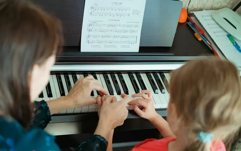 A teacher and a young student playing the piano together