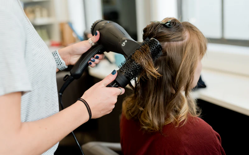 A hairstylist blow-drying a client's hair in a salon